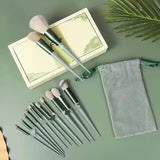 Set of makeup brushes with a green handle on a green surface, accompanied by a small notebook and a green drawstring bag.