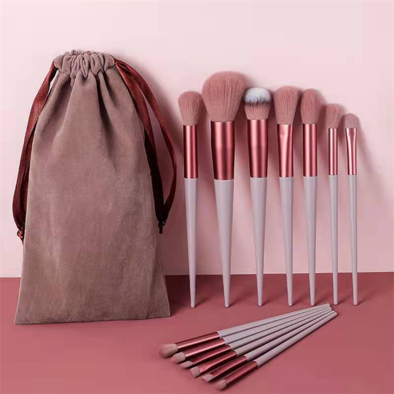 Set of makeup brushes with a brown drawstring bag on a pink background