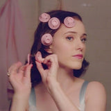 Woman with hair in pink rollers applying makeup in a bathroom.